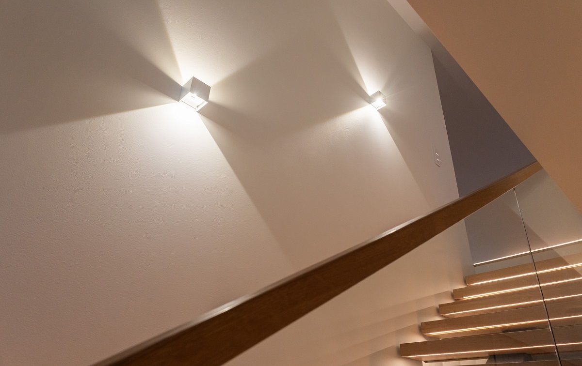 L'apparecchio a parete FUNKit illumina l'alta parete bianca della scala con un fascio di luce nitido verso l'alto e verso il basso.